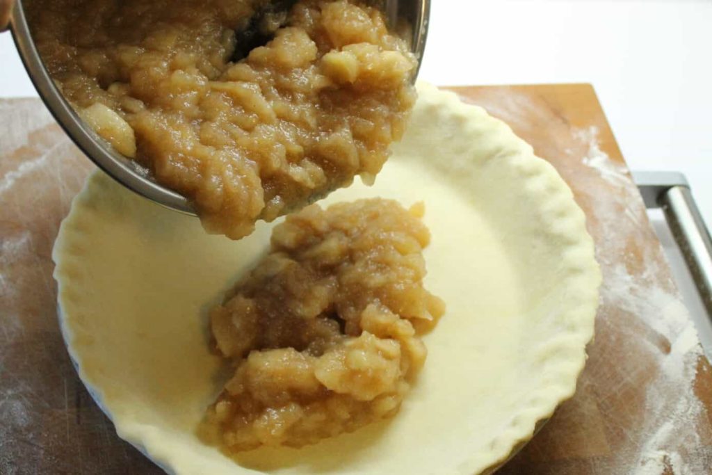 a unbaked pie shell being filled with homemade apple pie filling