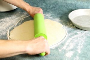 pie dough being rolled out on a floured blue countertop