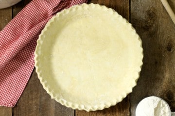 an overhead view of from scratch pie dough with crimped edges on a wooden table