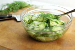 A glass bowl filled with german cucumber salad, garnished with fresh dill