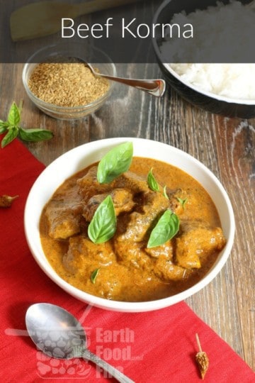 a bowl of beef korma curry on a wooden tabletop with a red napkin