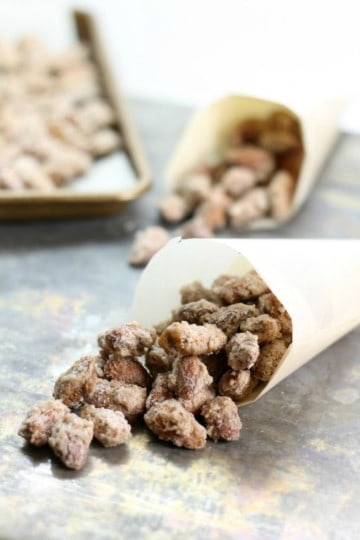 A cone of freshly baked sugar candied almonds on a table with a baking tray in the background.