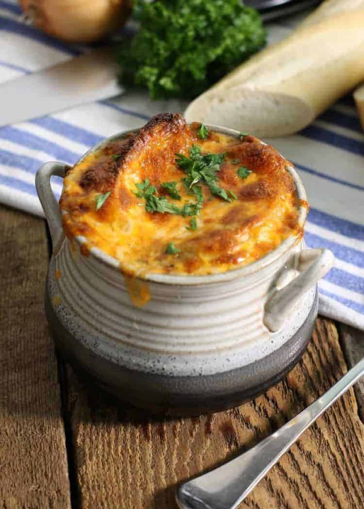 a stoneware style bowl filled with classic french onion soup topped with two croustinis and broiled cheese