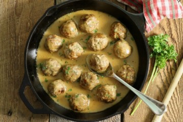 a cast iron pan filled with gluten free swedish meatballs on a barn board back board