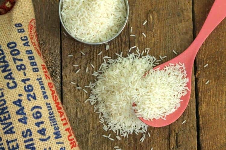 uncooked basmati rice spilling from a red spoon on a barnboard tabletop