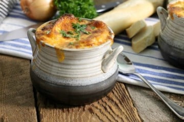 A grey stoneware bowl filled with french onion soup and topped with golden baked cheese.