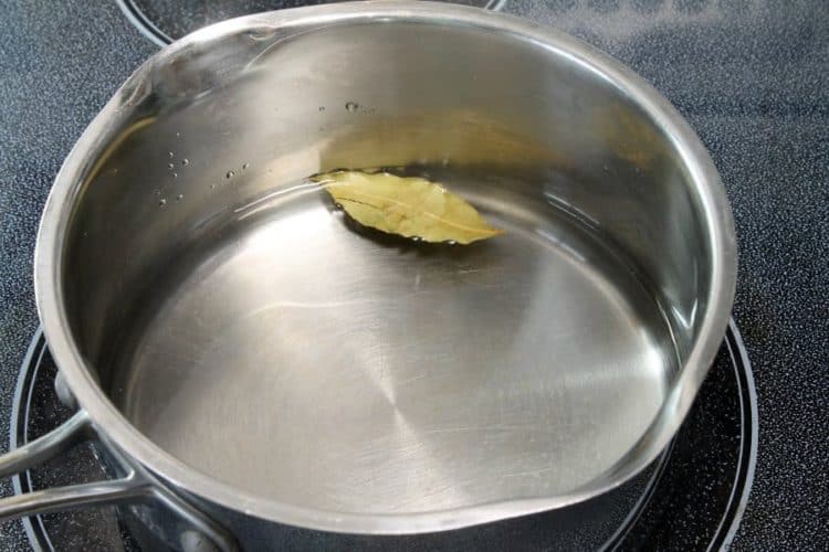 a pot of water with a bay leaf that will be used to cook basmati rice on the stove top