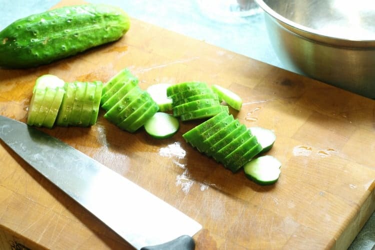 sliced cucumbers on a wooden cutting board prior to pickling