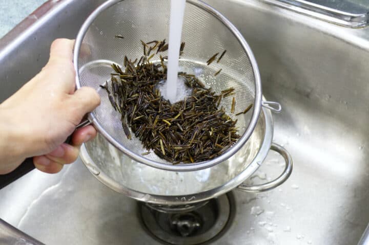 wild rice being rinsed in a mesh strainer under running water