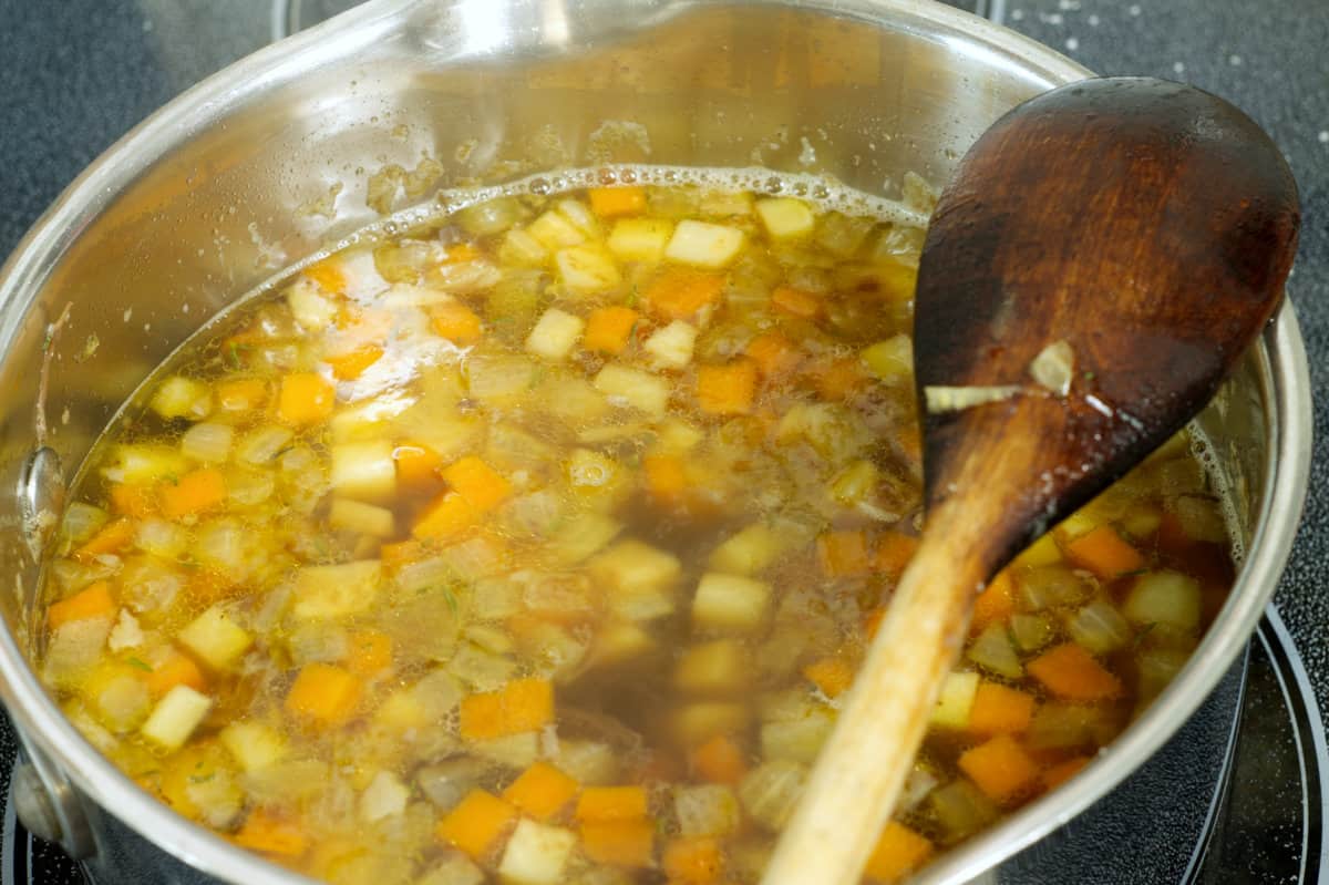 oxtail soup simmering in a pot with vegetable and herb garnishes