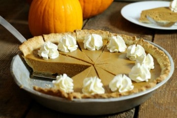 A sliced and garnished homemade pumpkin pie made from scratch, sitting on a wodden table . one pice of pie has been removed.