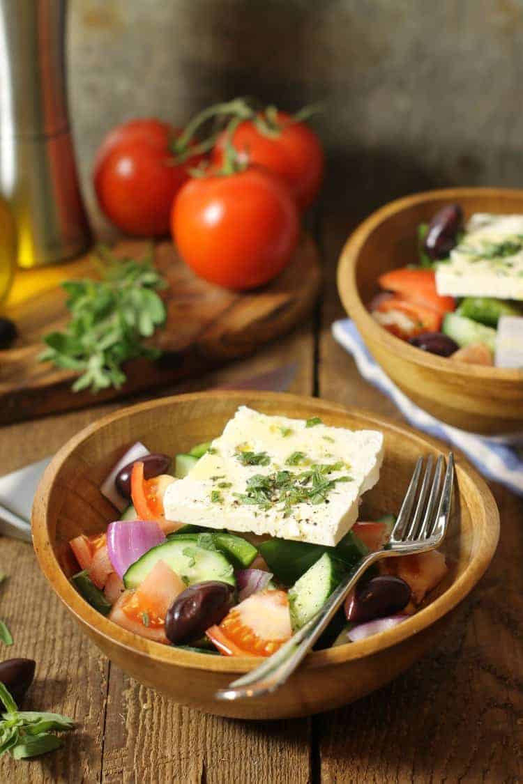 traditional greek salad (horiatiki) served in a wooden bowl with a thick slice of feta on top