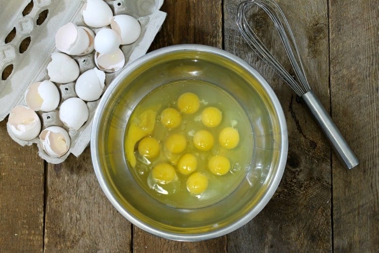 a dozen whole eggs cracked into a metal bowl