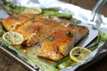 Brown sugar glazed salmon on a tinfoil lined pan surrounded by asparagus