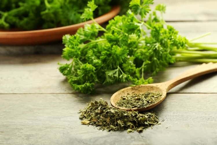 a bunch of fresh parsley as well as a spoon of dried parsley on a wooden table