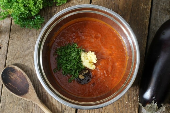 Tomato sauce being seasoned with herbs and spices