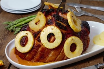 a honey a pineapple glazed ham on a serving platter with a carving fork stuck in the top