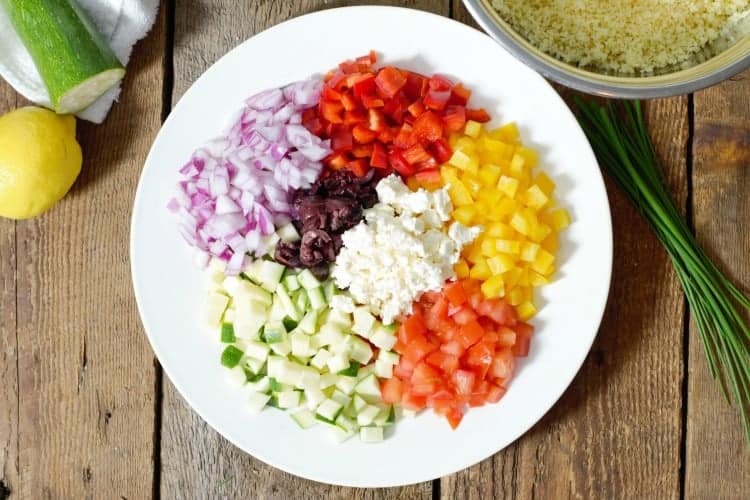 a plate of various diced vegetables including, zucchini, red onion, bell pepper, tomato, olive, and feta.