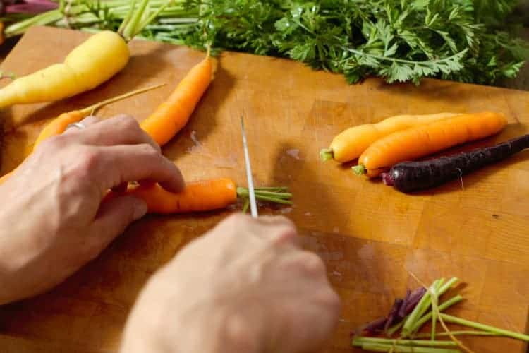 trimming carrot tops of off baby carrots with a chefs knife