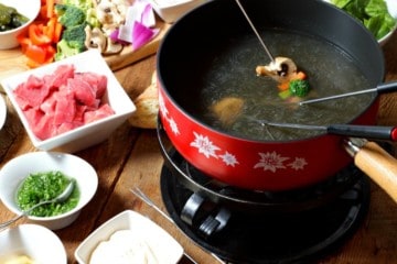 various food items being cooked in broth in a fondue pot