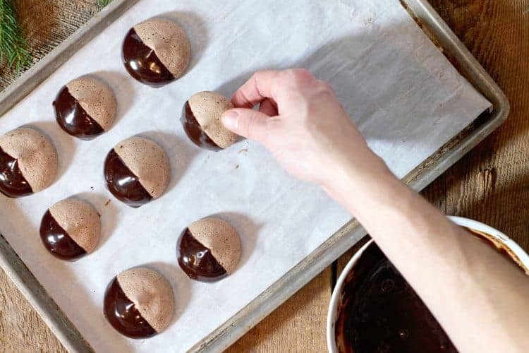 placing dipped chocolate meringue cookies on a sheet pan to set