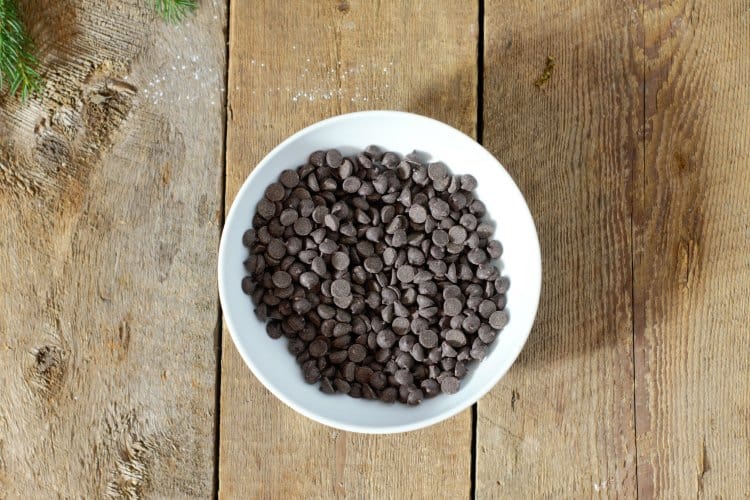 dark chocolate chips in a white procelain bowl on a barn board background