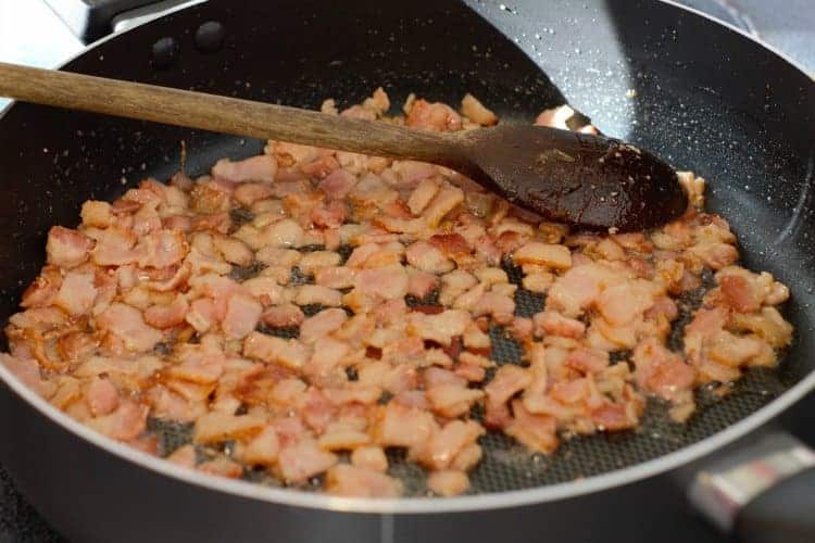 partially cooked diced bacon in a black pan