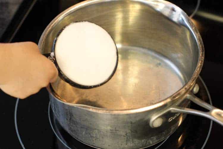 measuring out 1/2 cup of sugar in a pot