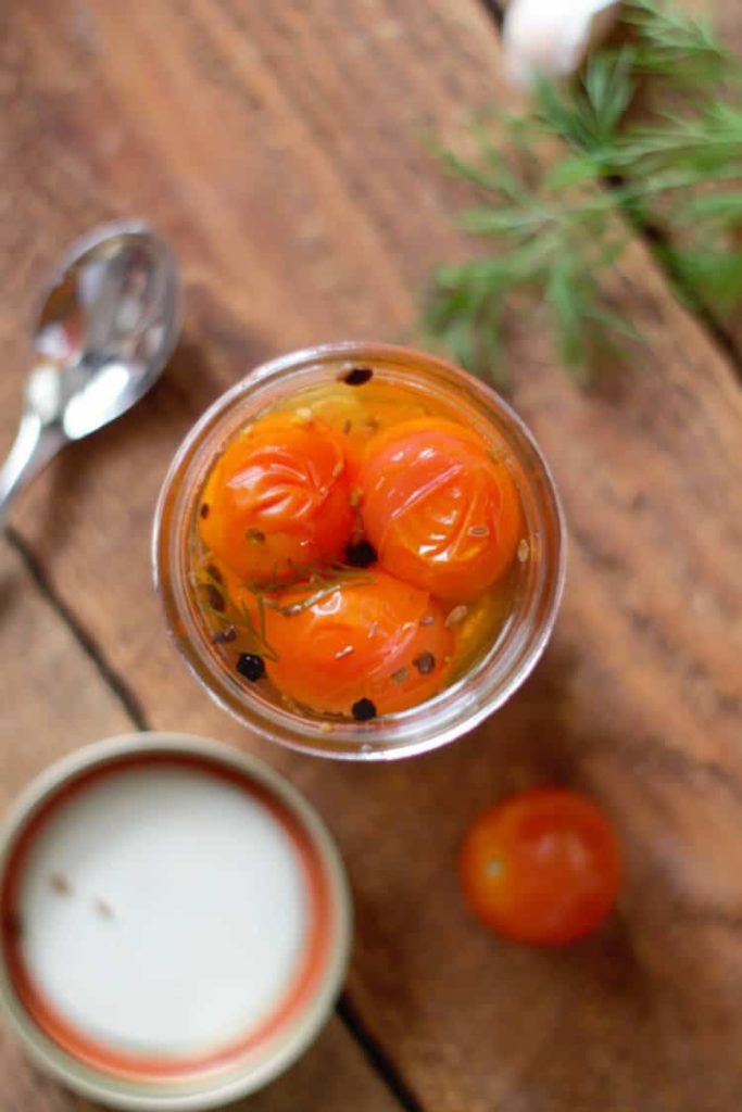 over head shot of pickled cherry tomatoes in an opened mason jar on a wood background