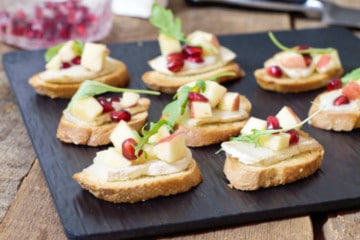 warm brie crostini's topped with a fresh apple and pomegranate salad on a black slate serving board