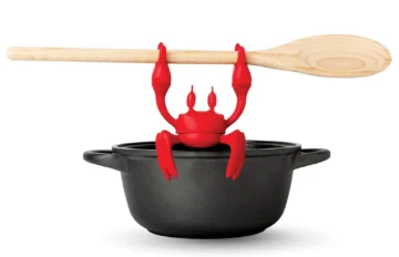 red silicone crab sitting on the black pot holding wooden spoon - Red the Crab Silicone Utensil Rest