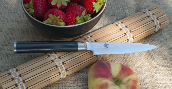 Damascus Stainless Steel Shun Classic 4" Japanese Paring Knife placed on the bamboo mat between strawberries and peach