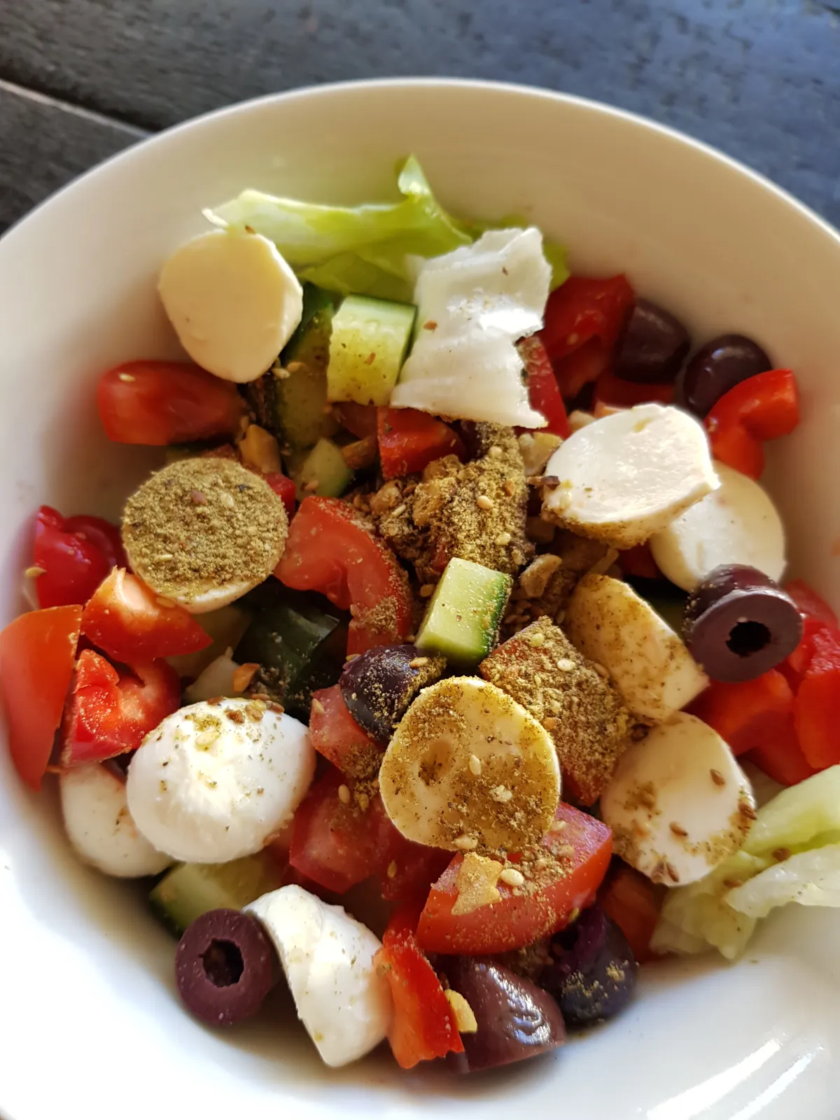 Dukkah sprinkled over salad with olives and bocconciny balls.